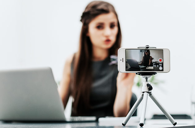 A woman filming with a smartphone mounted on a mini tripod.