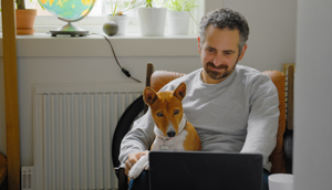 A man working on his laptop with a dog sitting on his lap.