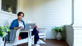 A woman working on a laptop on a porch.