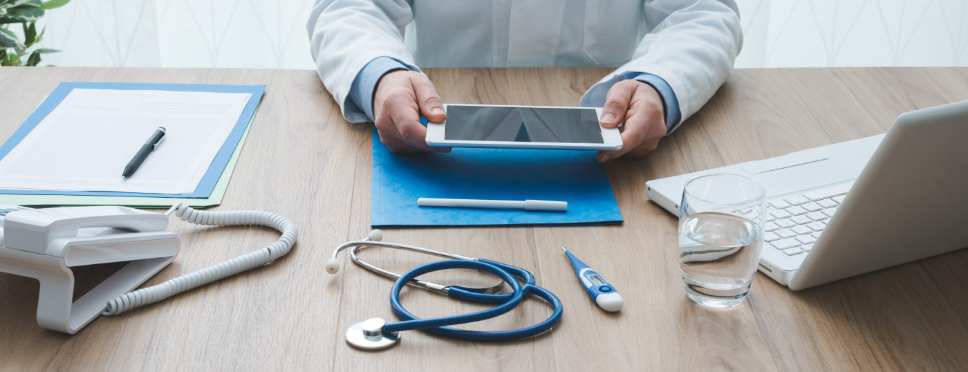A desk with a laptop, tablet, and a stethoscope.